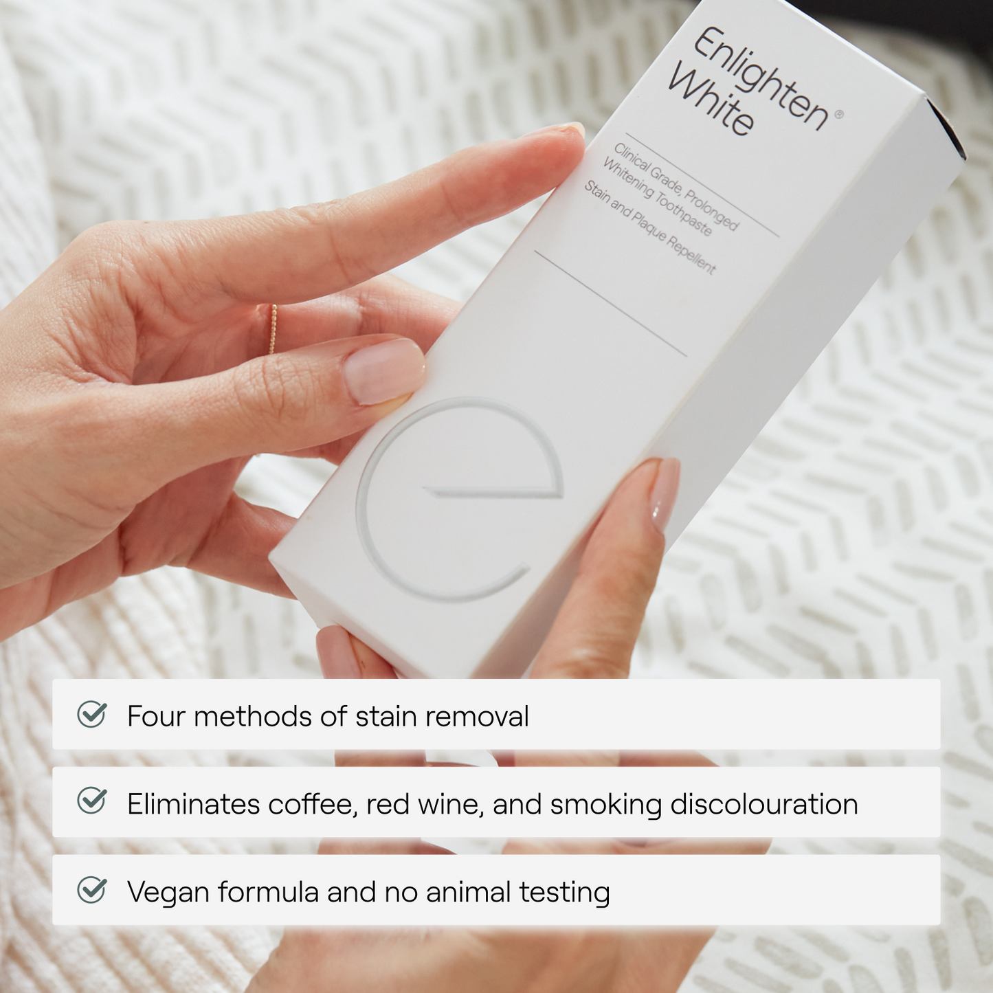 Hands holding Enlighten White toothpaste box displaying product benefits