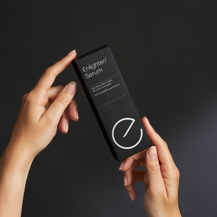 Hands holding Enlighten Serum toothpaste box