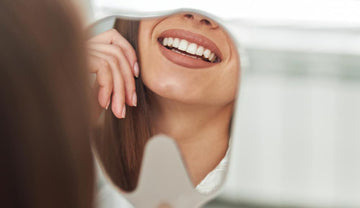 Oral Microbiome - a woman looking her white and clean teeth in a smile designed mirror