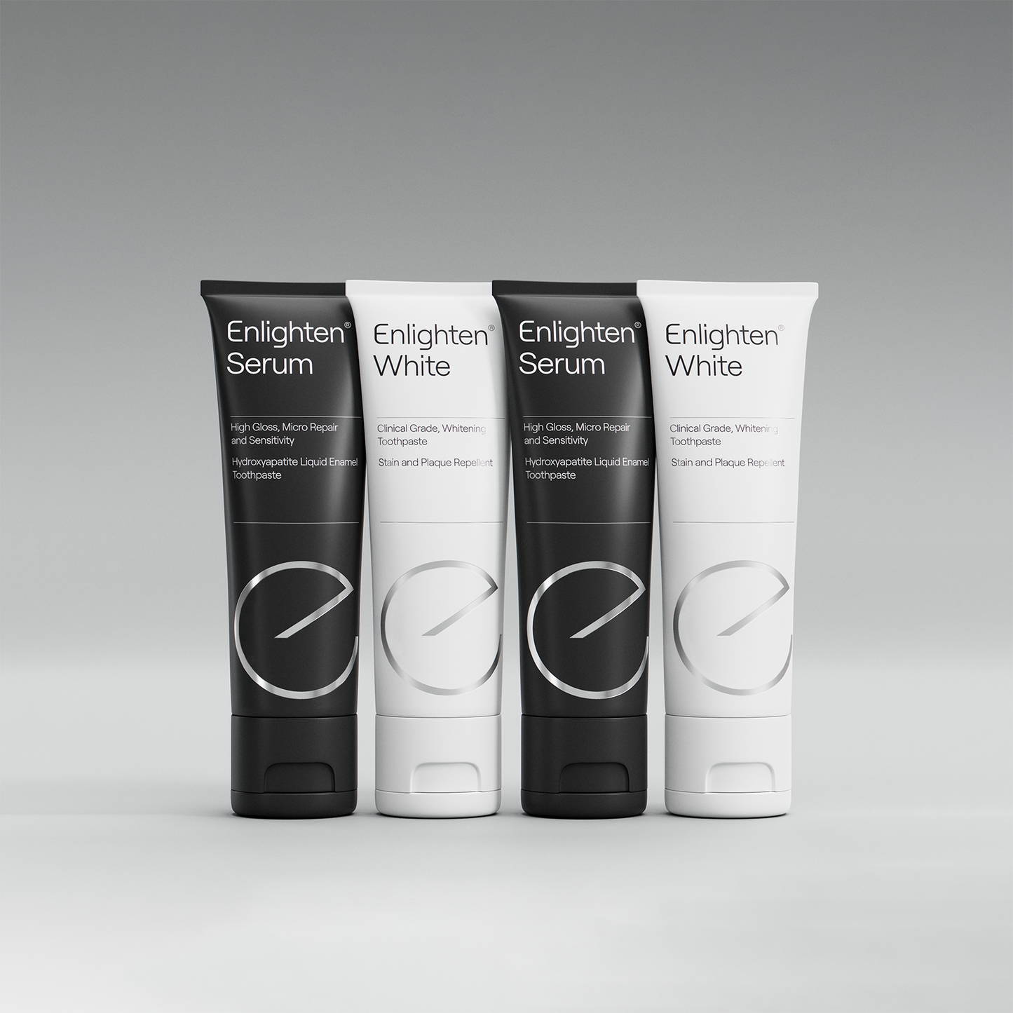 A display of four toothpaste tubes, alternating between Enlighten Serum (black) and Enlighten White (white). Each tube features the Enlighten logo and clear labelling: Enlighten Serum for sensitivity relief and enamel repair, and Enlighten White for clinical-grade whitening and plaque repellent. The tubes are neatly arranged against a neutral grey background, highlighting their sleek, minimalist design and premium quality.